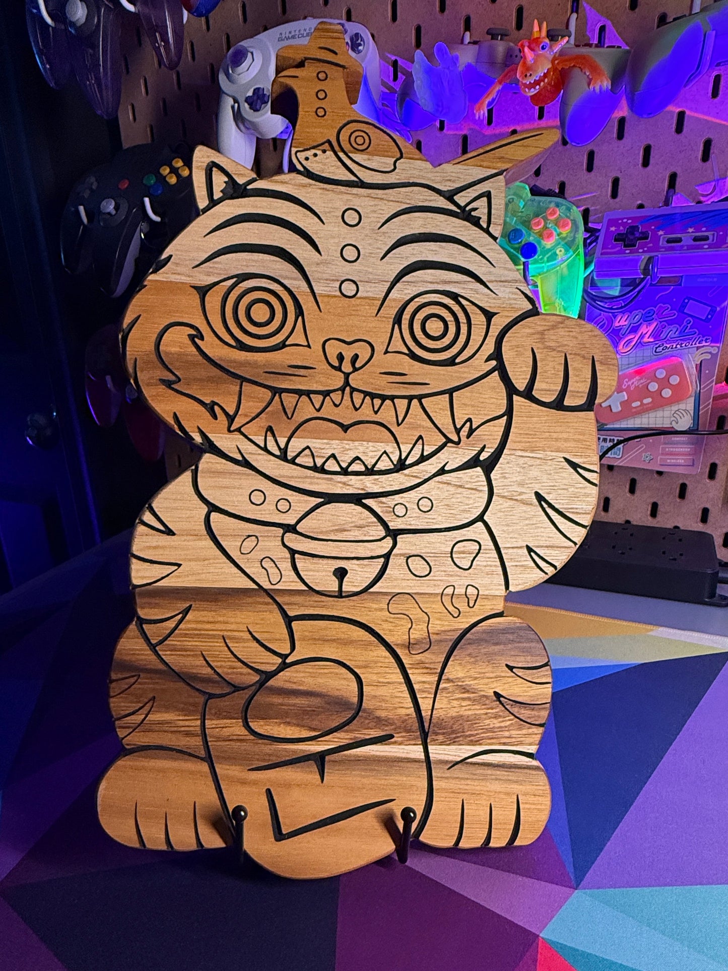 A handcrafted wooden cat figurine with intricate black line art and engraved patterns, displayed on a colorful geometric surface in a decorated room.